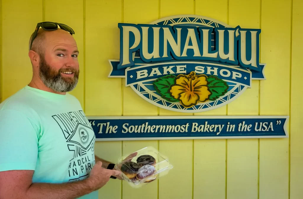 Tom in front of Punalu'u Bake Shop with malasadas on the Big Island of Hawai'i.