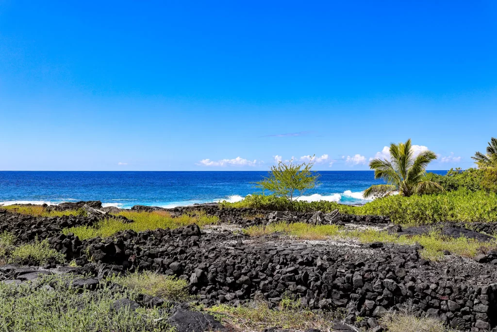 Remnants of a black basalt rock wall with the Hawaiian Pacific Ocean in the background.