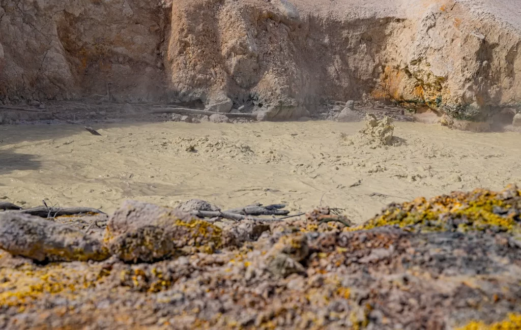 Mudput surrounded by rough hardened lava and colored yellow with sulphur.