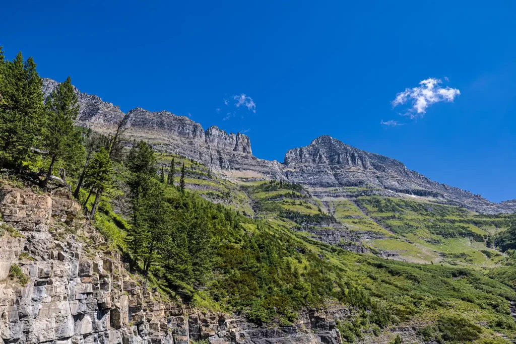 A tall granite ridgeline rises above Bird Woman Falls in Glacier National Park.