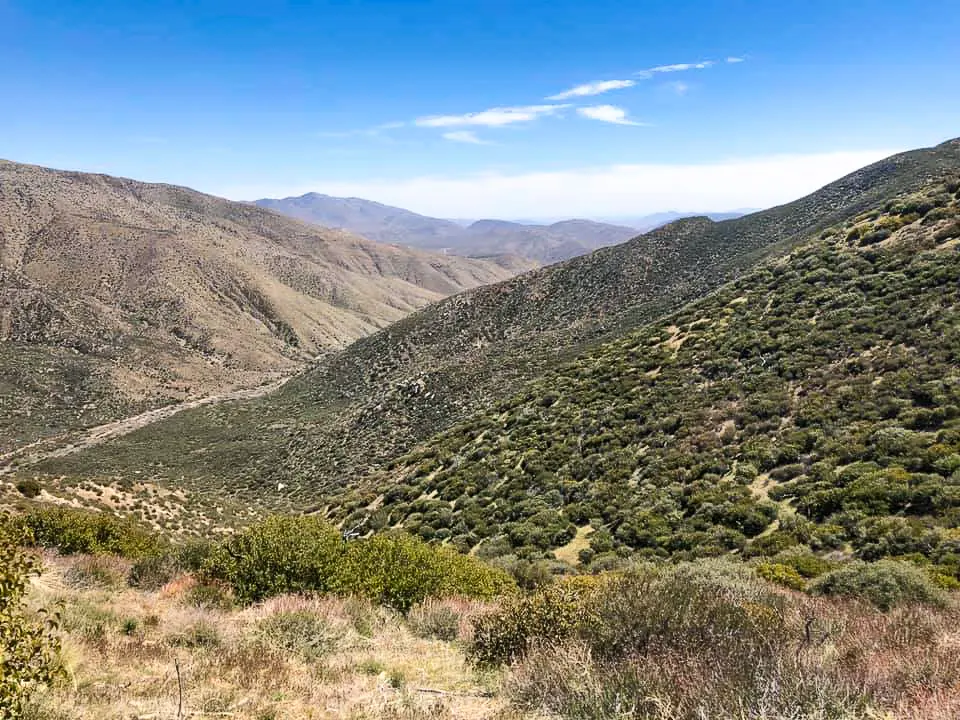 The PCT overlooks a green valley surrounded by rolling hills.