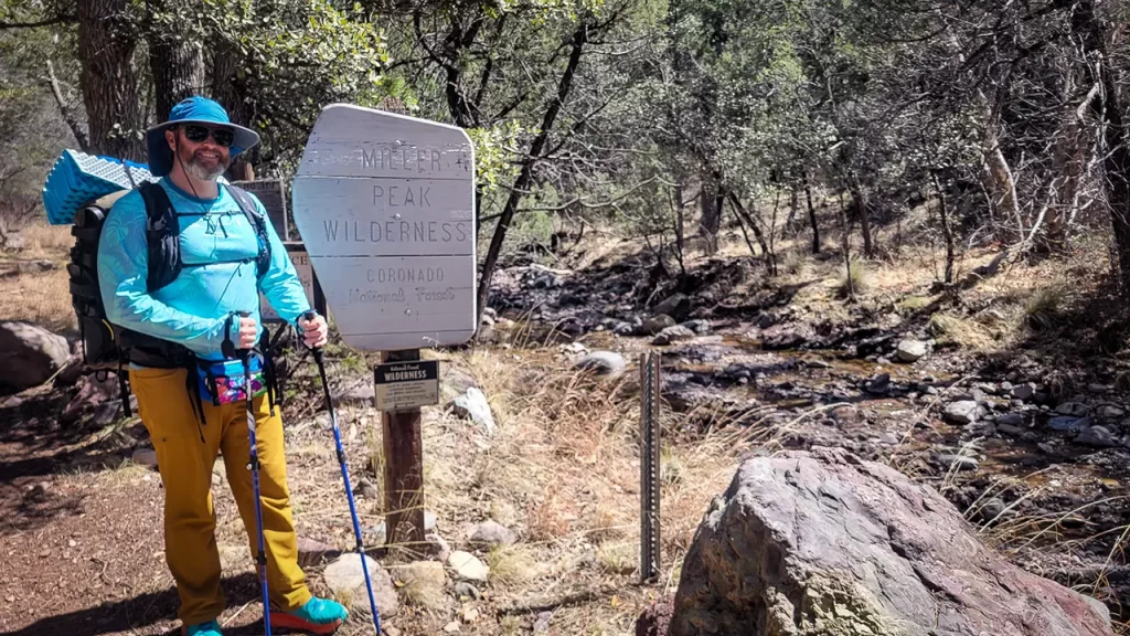 Tom standing in front of a sign for Miller Peak in Coronado National Forest.