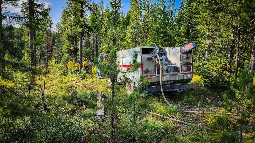 A small fire truck and group of firefighters put out a small fire.